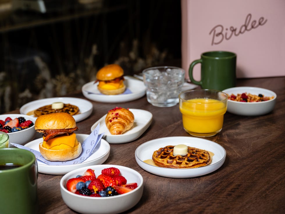 A spread of breakfast items including sliders, waffles, fruits, croissants, and drinks on a wooden table. A spread of breakfast items including sliders, waffles, fruits, croissants, and drinks on a wooden table.