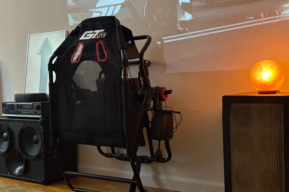 Racing simulator seat positioned next to speakers and a lamp, with a projector displaying images on the wall.