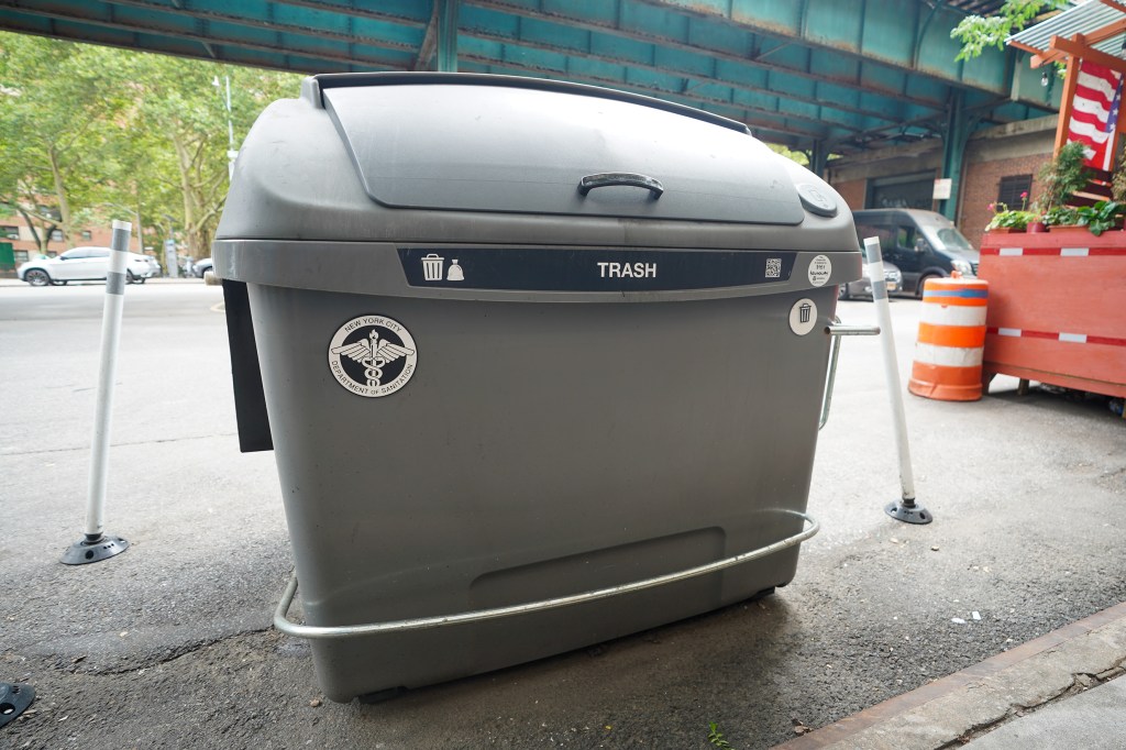 An Empire Bin, a large gray trash container with a "TRASH" label and the New York City Department of Sanitation logo, sits on a sidewalk near El Porton Mexican Restaurant at 3151 Broadway in Manhattan.