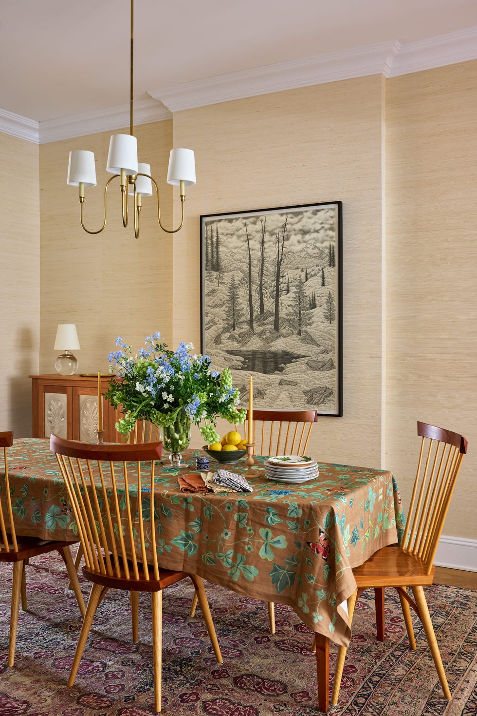 Brightly decorated dining room featuring a wooden table, floral centerpiece, and a landscape painting on the wall.