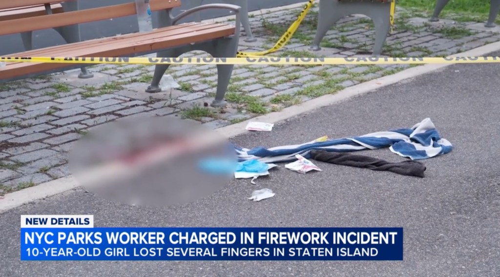 A park bench with yellow caution tape, and debris on the ground including a blue and white striped towel, a gray towel, and other small items; a blurred circle obscures a portion of the ground, with text "NYC PARKS WORKER CHARGED IN FIREWORK INCIDENT 10-YEAR-OLD GIRL LOST SEVERAL FINGERS IN STATEN ISLAND" at the bottom.