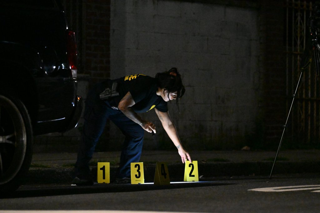 NYPD officer marking evidence with numbered tents at the scene of a fatal shooting.