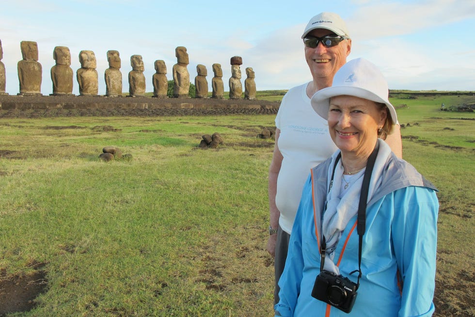 Couple posing in front of Easter Island's Moai statues on a grassy landscape under a clear sky.
