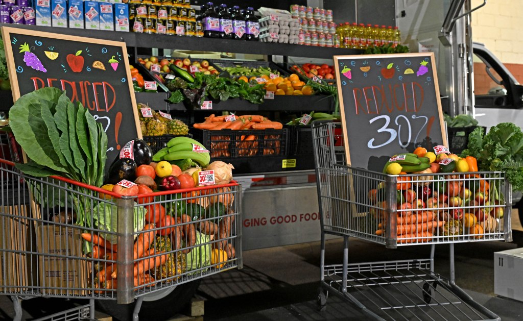 Two shopping carts filled with produce are next to chalkboards advertising 30% reduced prices.