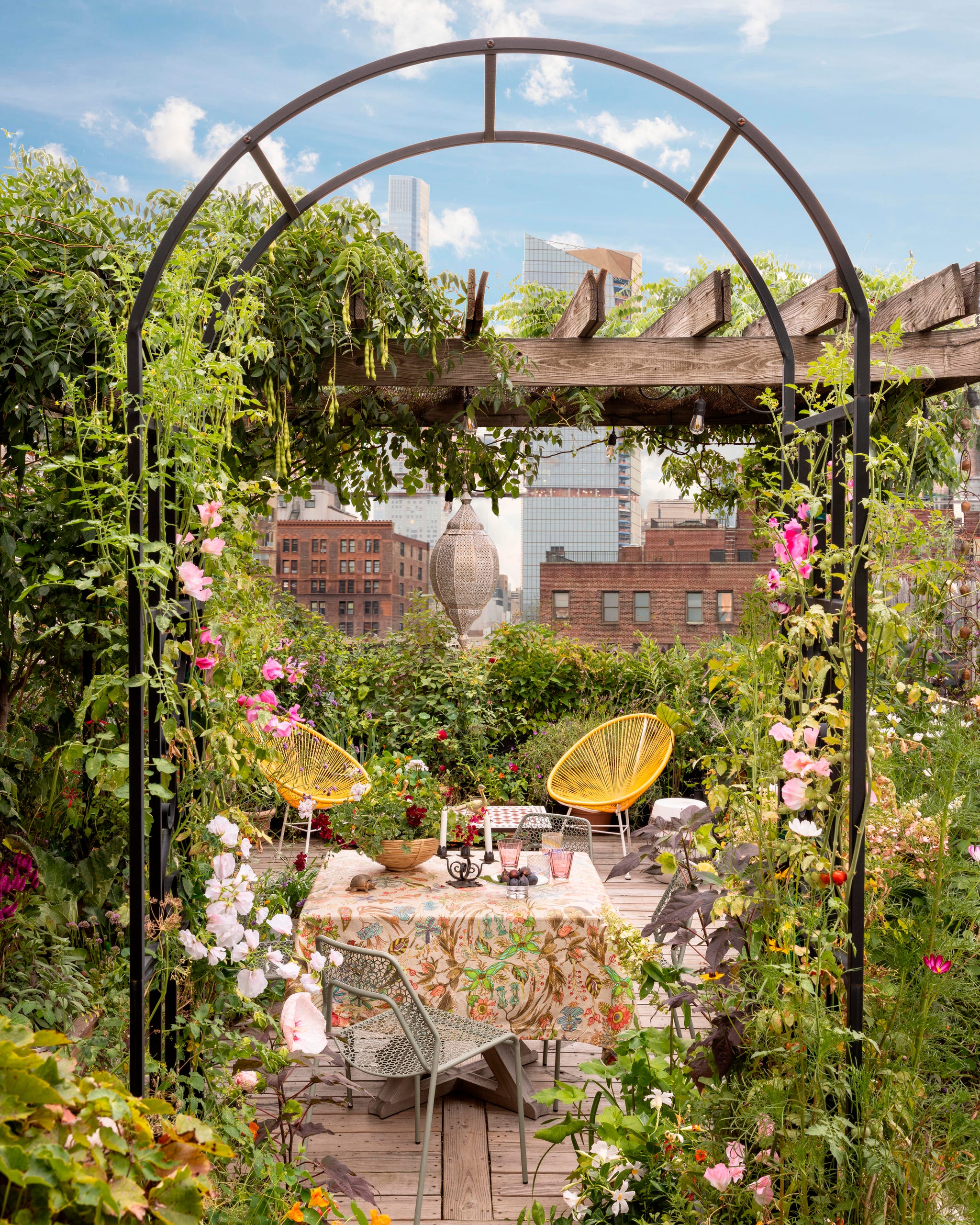 A vibrant rooftop garden with colorful flowers, a wooden deck, and stylish seating, set against a city skyline.