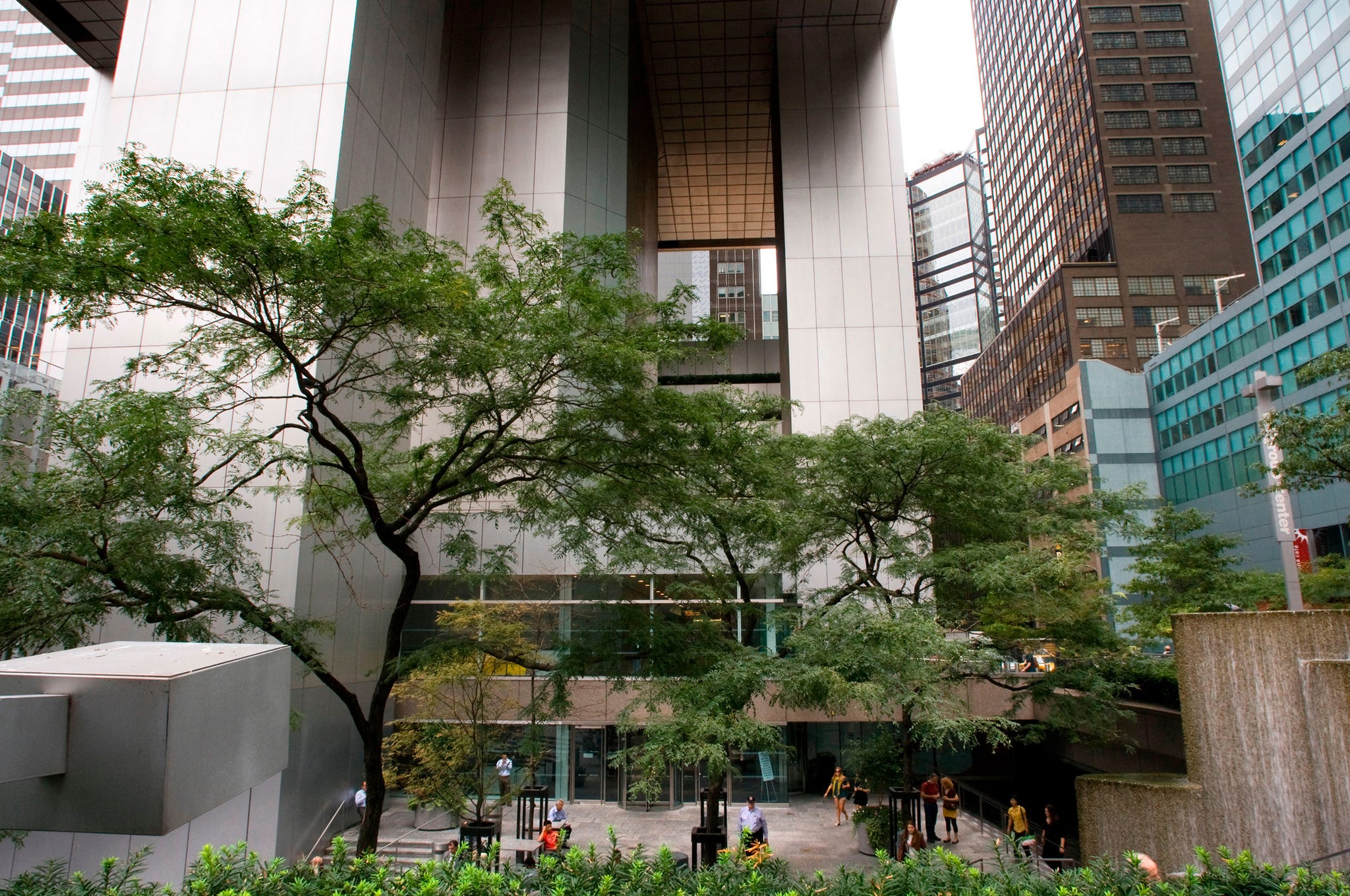 Modern urban architecture with trees and a plaza in a bustling city environment.