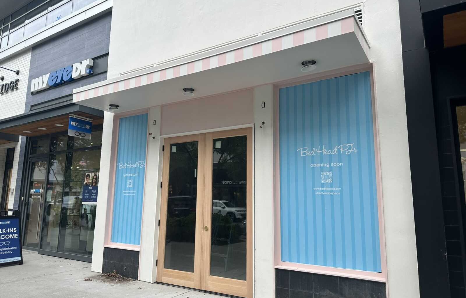 Storefront with a pink-striped awning and glass double doors; blue window panels read 'Bed Head PTs opening soon.'