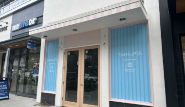 Storefront with a pink-striped awning and glass double doors; blue window panels read 'Bed Head PTs opening soon.'