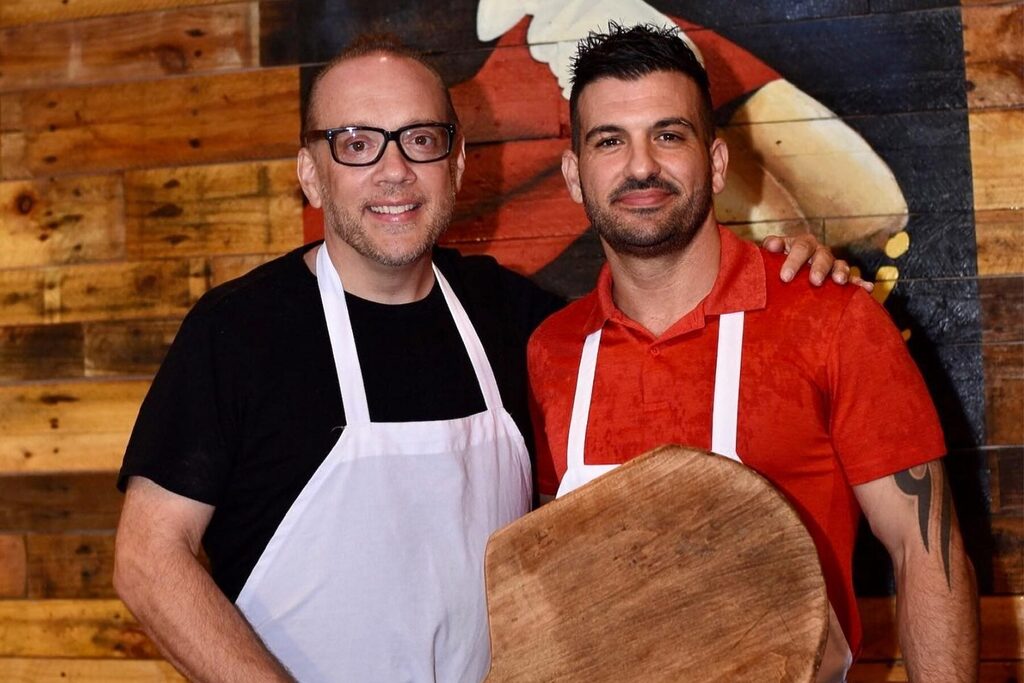 Bruno DiFabio and Mike Bennici, wearing aprons and holding a pizza pallet.