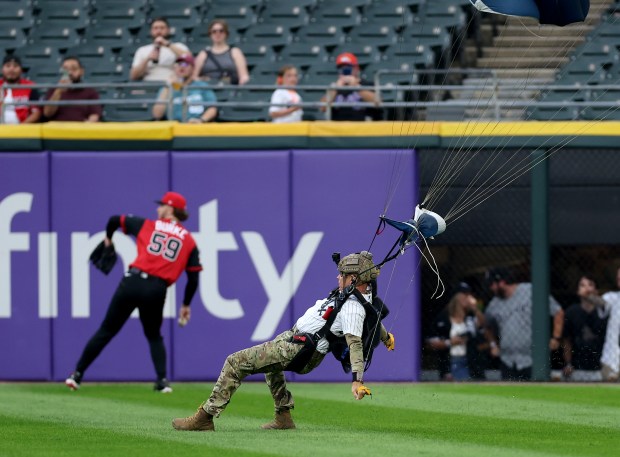A parachute jumper lands in the outfield as White Sox starter Sean Burke (59) warms up for a game against the Mets on Aug. 21, 2026, at Rate Field. (Chris Sweda/Chicago Tribune)