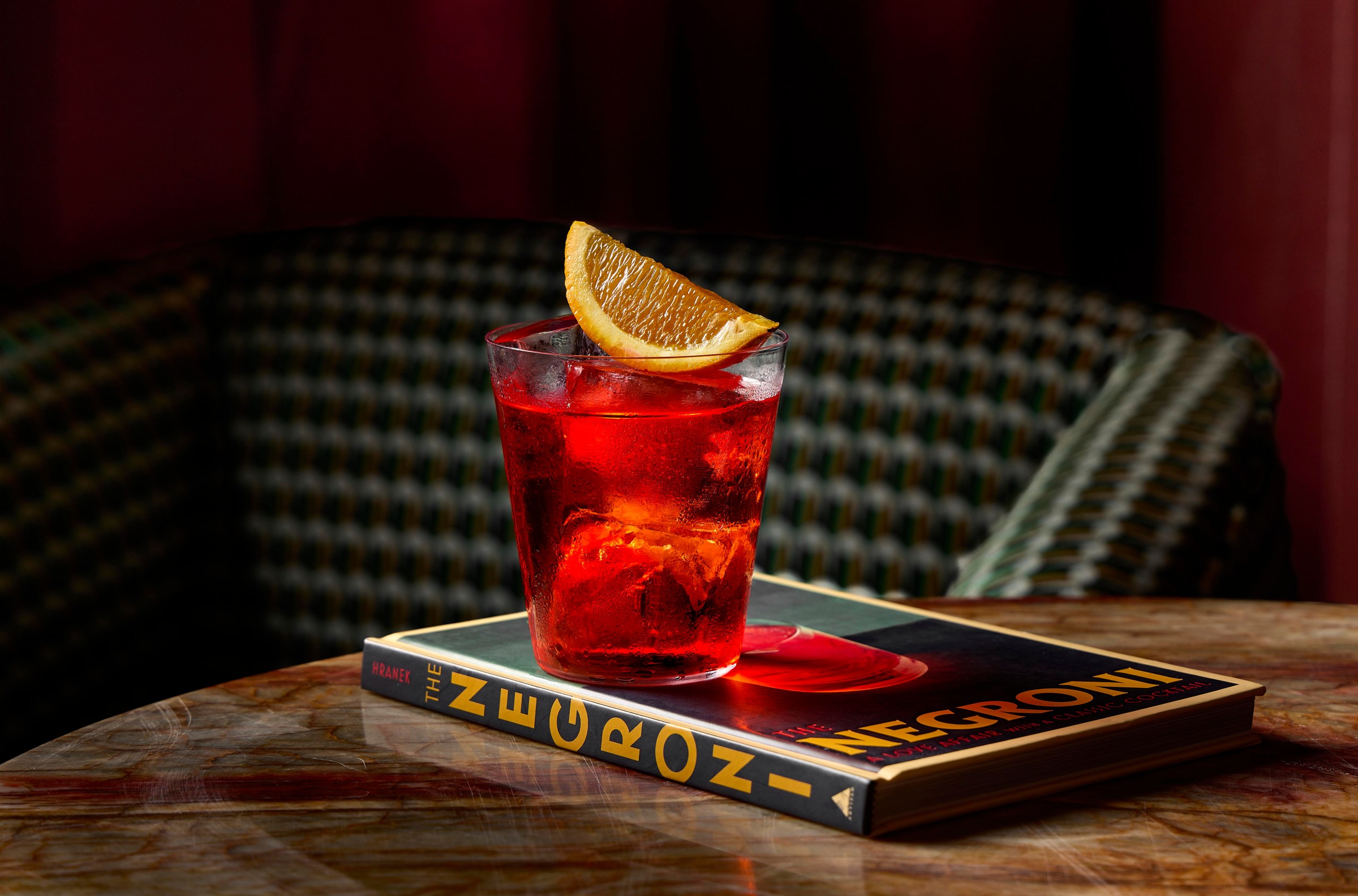 A red cocktail with an orange slice on top of a book reading Negroni.