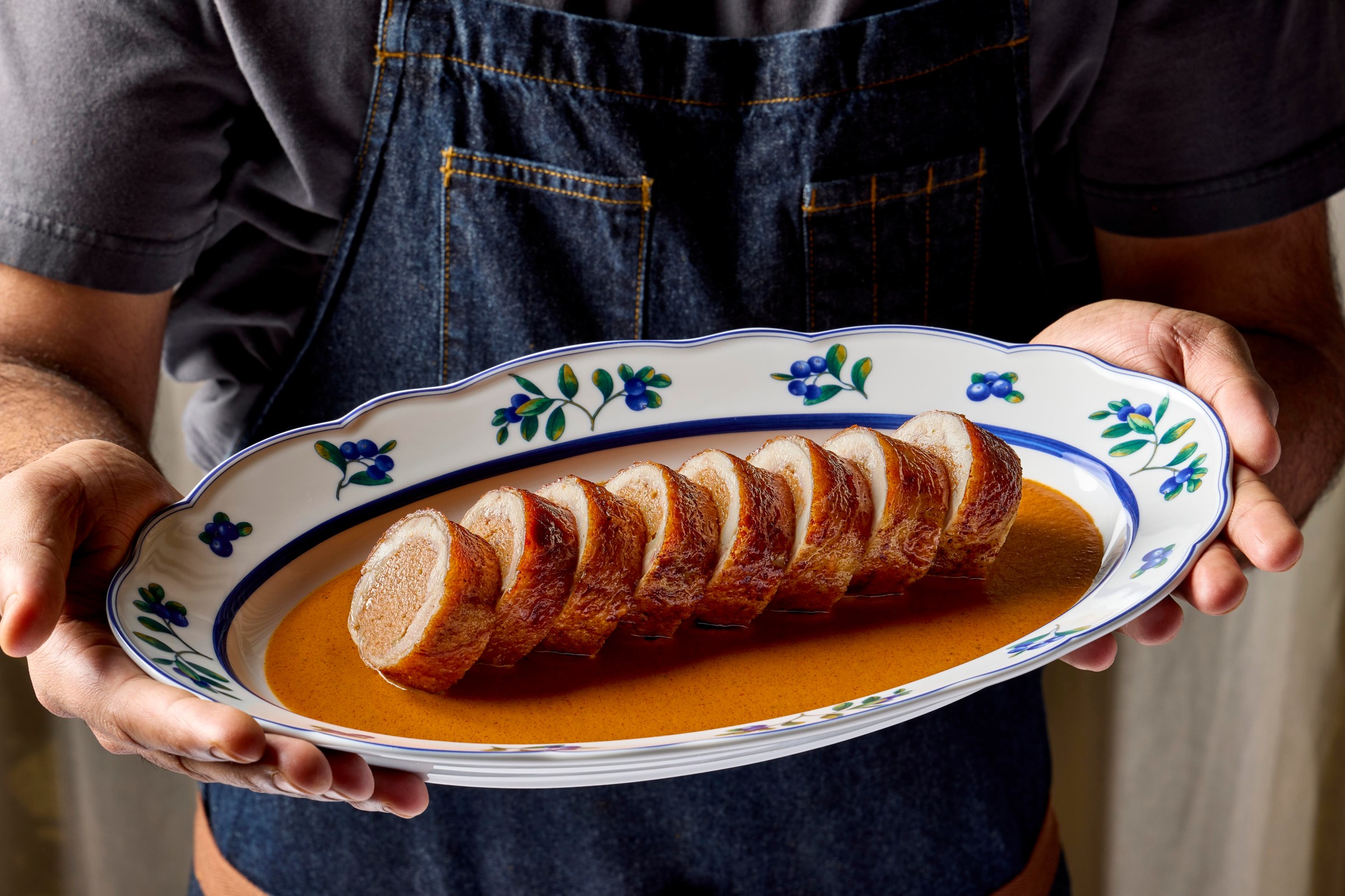 Someone holding up a sliced-rolled-up meat thing with sauce.