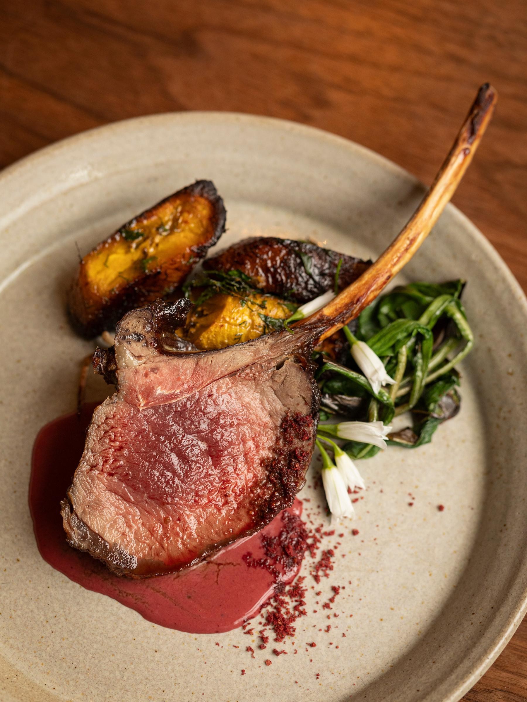 A bone-in meat chop on a plate with sauce and greens.