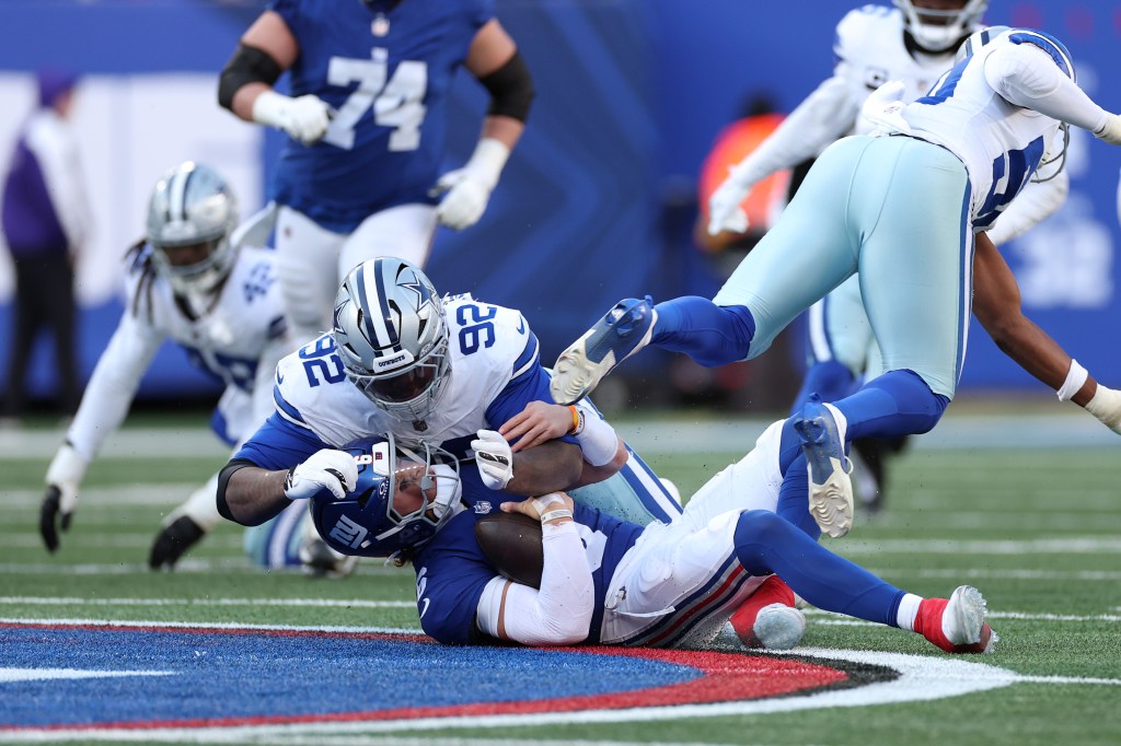 Dallas Cowboys player tackles a New York Giants player, who is holding the football.