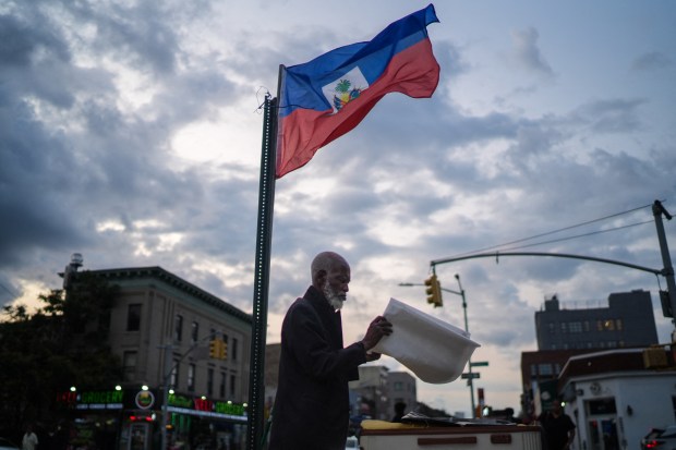 A man works at a table below a Haitian flag in the Little Haiti neighborhood of Brooklyn, New York, on July 29, 2026. (Photo by Ryan MURPHY / AFP via Getty Images)