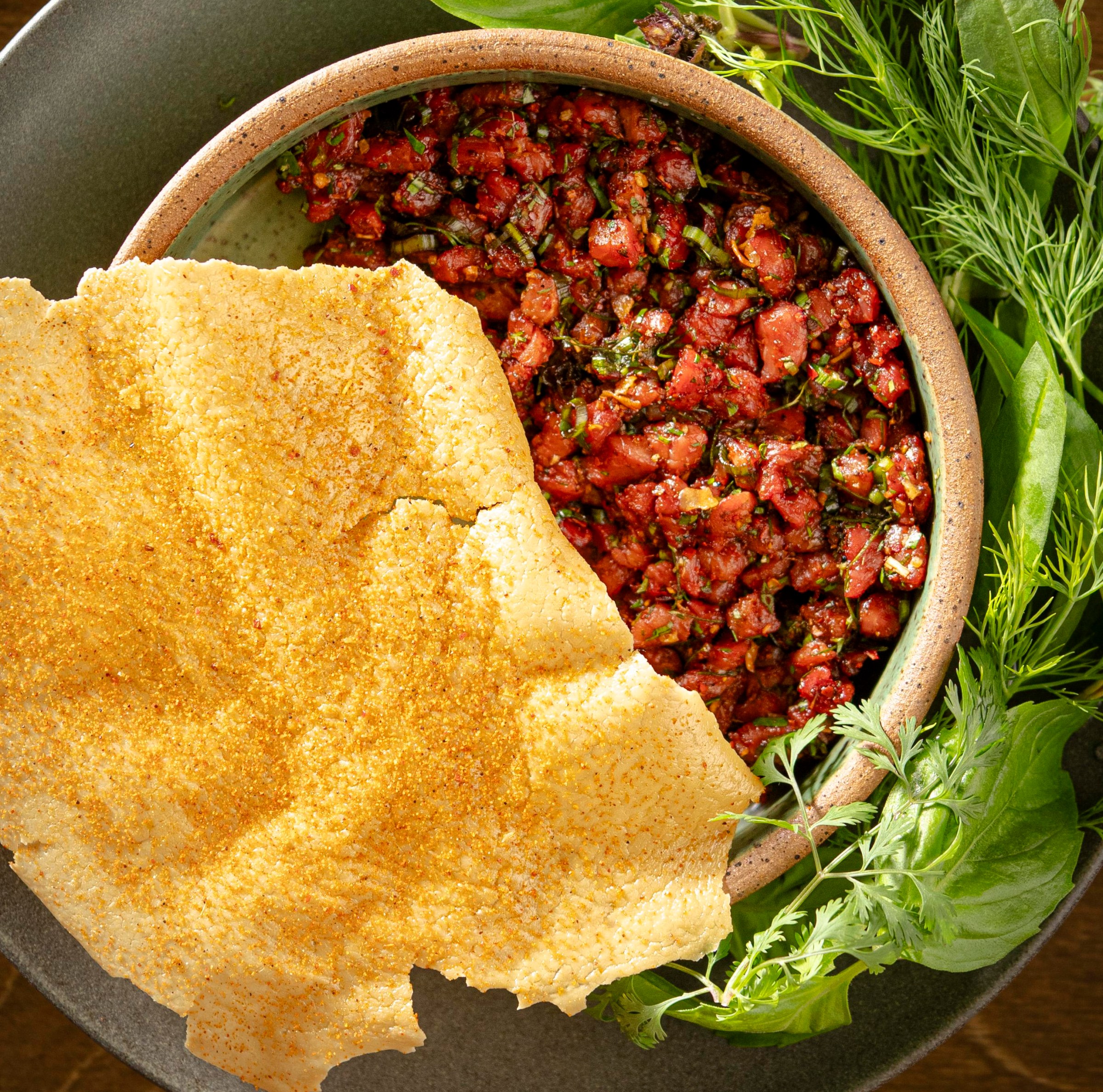 A bowl of tartare on top of greens with a huge cracker on top of it.