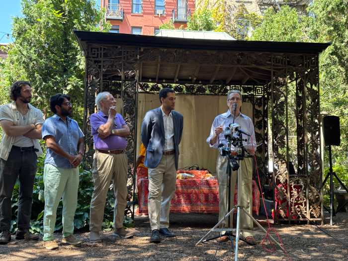 five men standing around a microphone outside in a garden