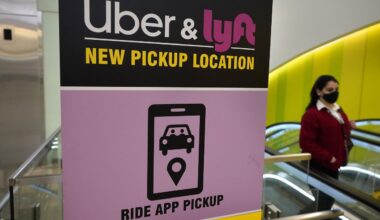 In this Feb. 9, 2021 file photo, a passer-by walks past a sign offering directions to an Uber and Lyft ride pickup location at Logan International Airport, in Boston. Thousands of U.S. ride-hailing workers plan to park their cars and picket at major U.S. airports Wednesday, Feb. 14, 2024, in what organizers say is their largest strike yet in a drive for better pay and benefits. (AP Photo/Steven Senne, File)