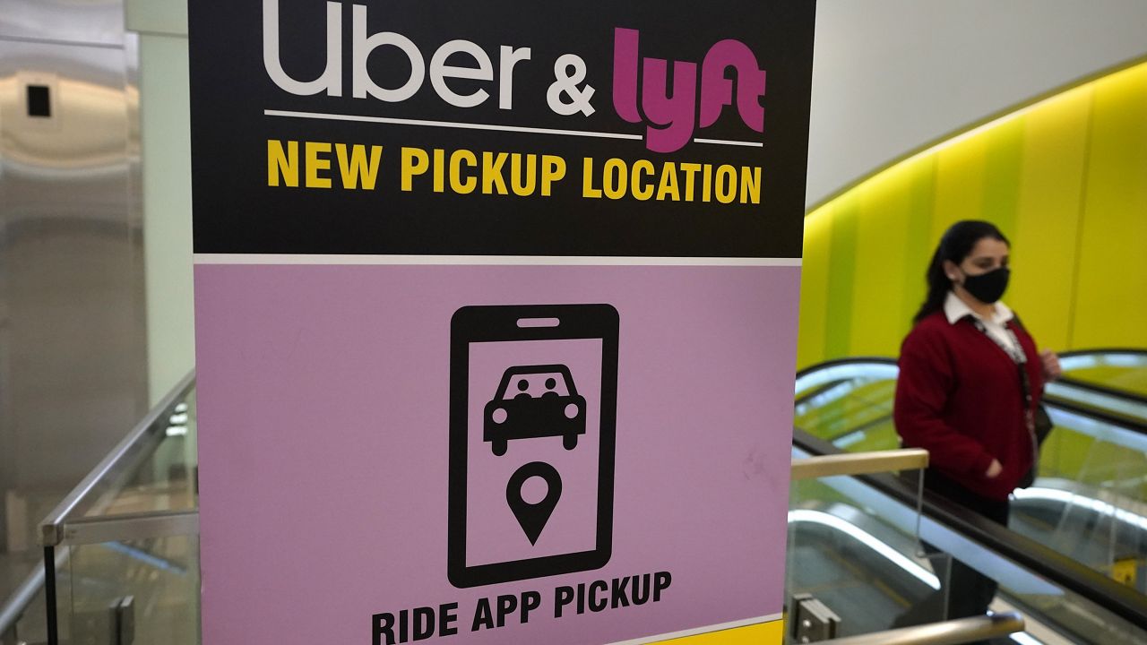 In this Feb. 9, 2021 file photo, a passer-by walks past a sign offering directions to an Uber and Lyft ride pickup location at Logan International Airport, in Boston. Thousands of U.S. ride-hailing workers plan to park their cars and picket at major U.S. airports Wednesday, Feb. 14, 2024, in what organizers say is their largest strike yet in a drive for better pay and benefits. (AP Photo/Steven Senne, File)