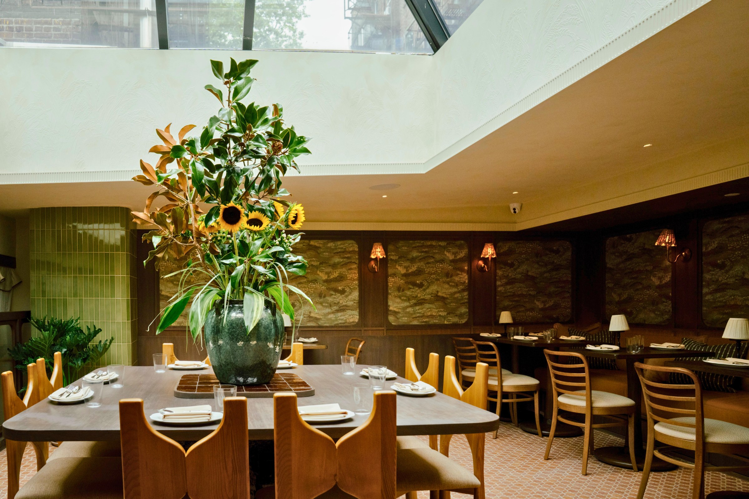 A dining room with a large table in the middle with a vase of sunflowers.