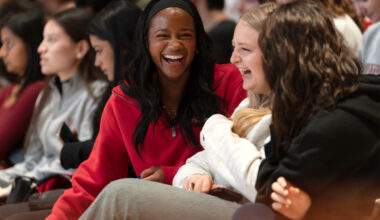 Three students seated in the crowd laugh together during the ceremony.