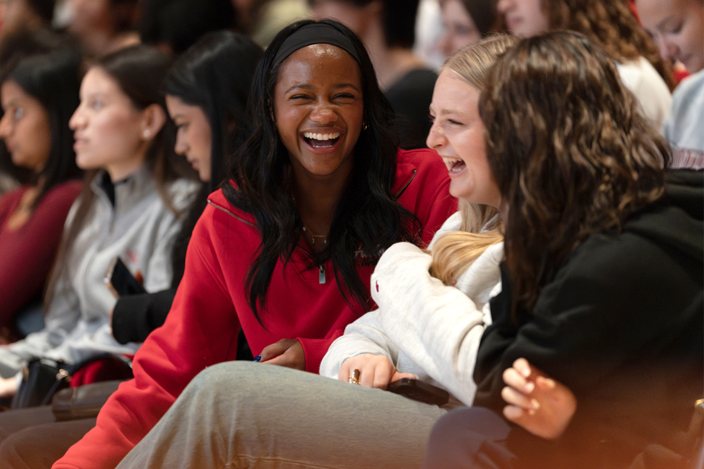 Three students seated in the crowd laugh together during the ceremony.