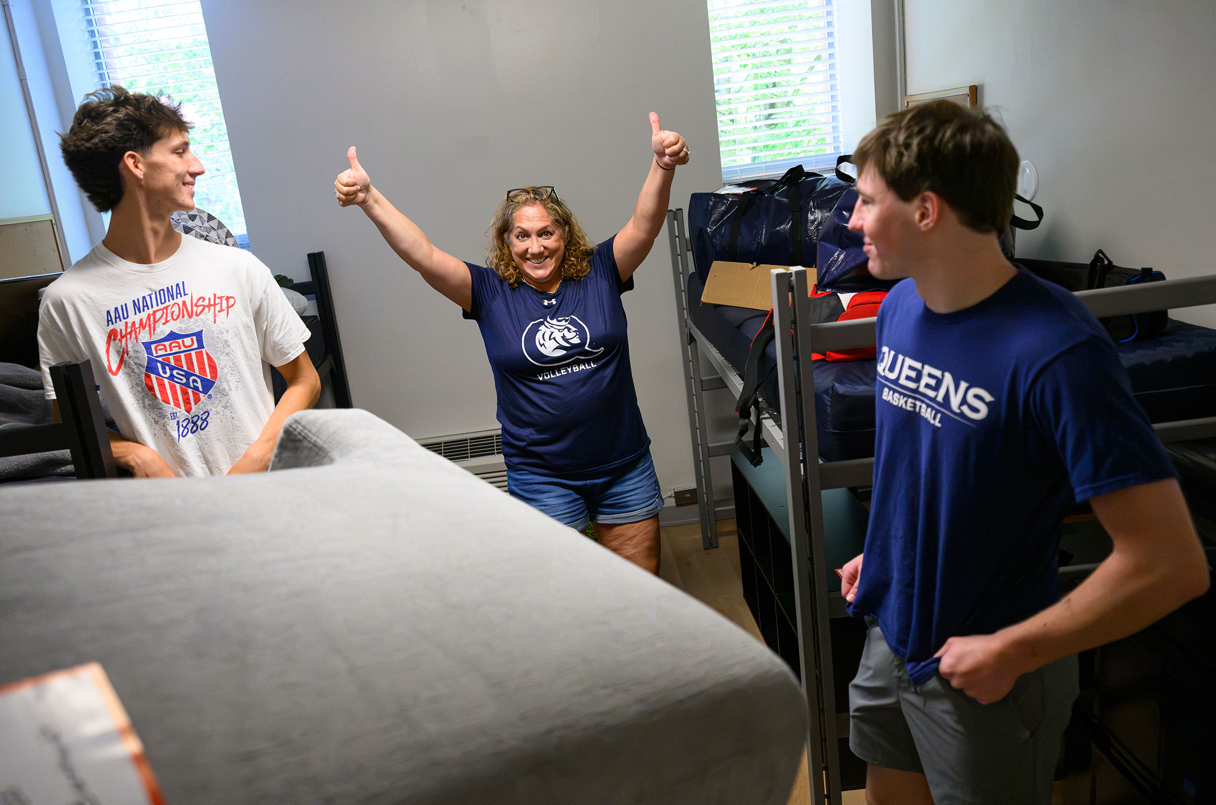 A woman wearing a blue Queens University teeshirt gives the thumbs up in a student room.