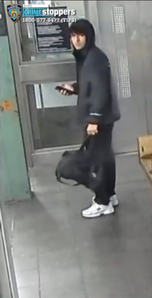 CCTV image of a male suspect wearing a black hoodie, black pants, white shoes, and holding a phone and a black bag.