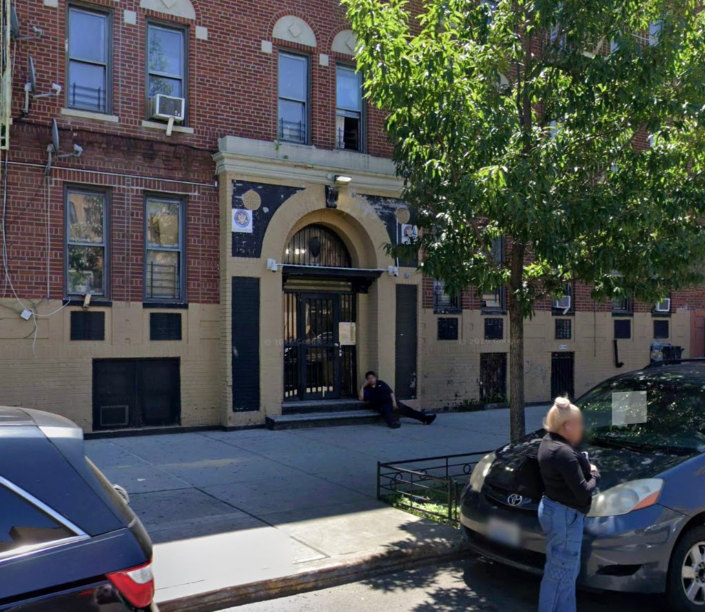 A female lying on the steps of 1236 Grand Concourse in front of a brick building.