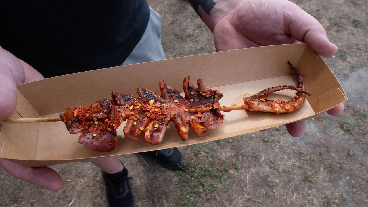 A fairgoer holds a grilled squid.