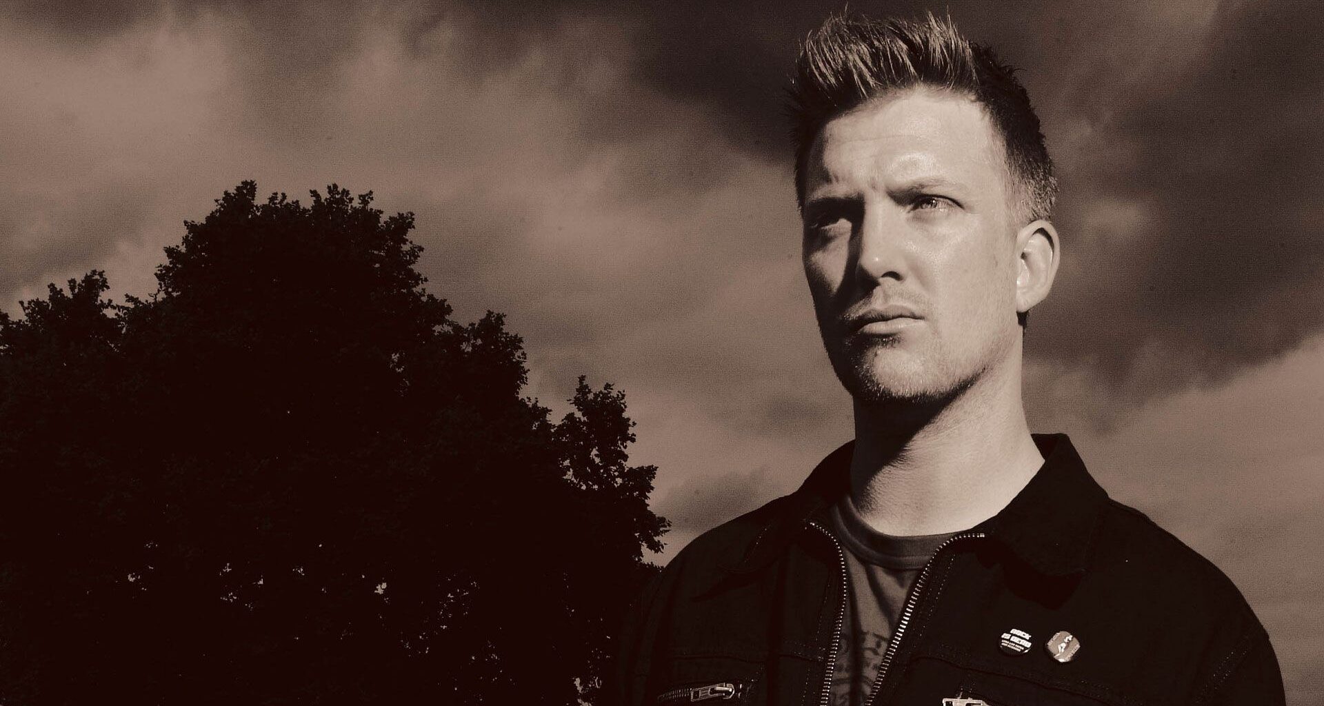 A sepia portrait of Josh Homme in a field next to a tree