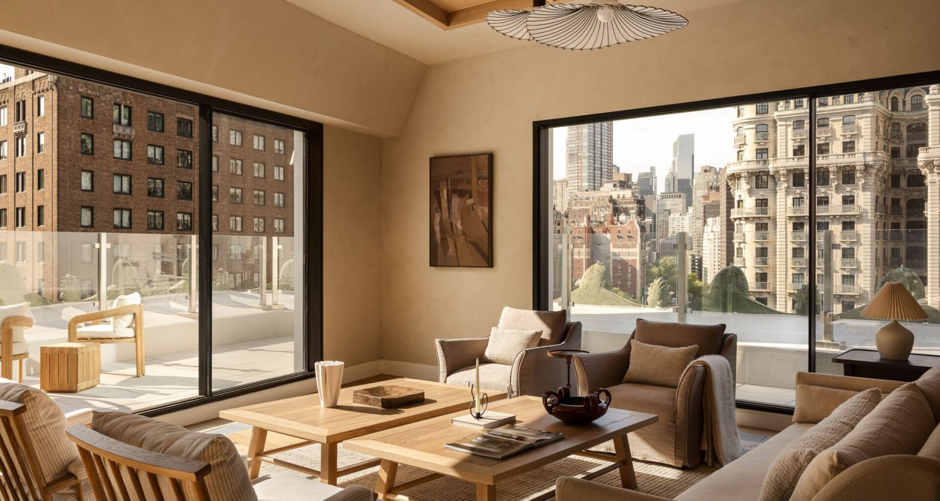 A neutral living room in a penthouse with a balcony running around it with a glass balustrade with two matching wood coffee tables in the center of mirroring armchairs and a sofa