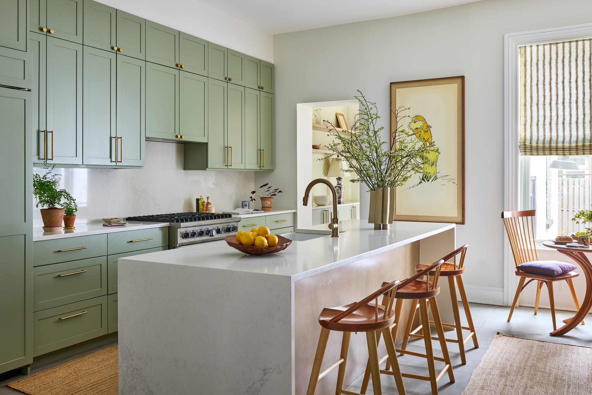 Modern kitchen with green cabinetry, marble island, bar stools, and natural light illuminating a cozy dining area.