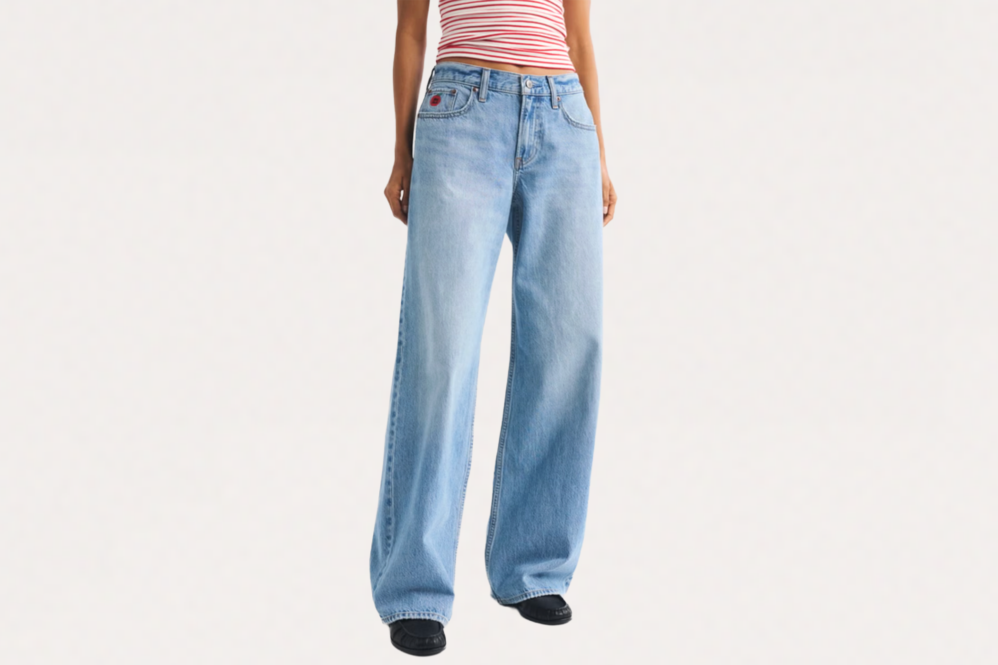 A person wearing baggy light wash jeans and a striped crop top.