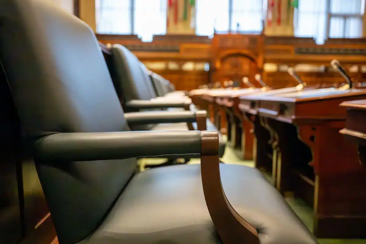 A gavel resting on a bench in an empty courtroom, morning light filtering through tall windows, dust particles visible in the rays, suggesting legal proceedings and institutional power