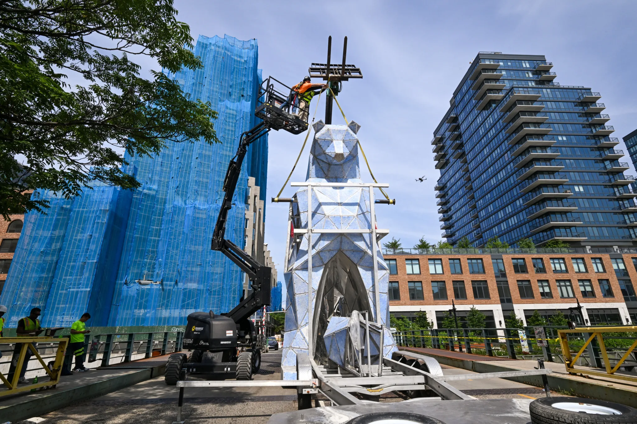 Workers on lift installing geometric animal sculpture by Jen Lewin in urban area with skyscrapers.