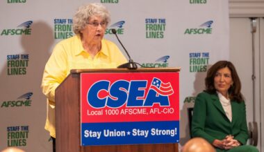 woman speaks at podium alongside governor
