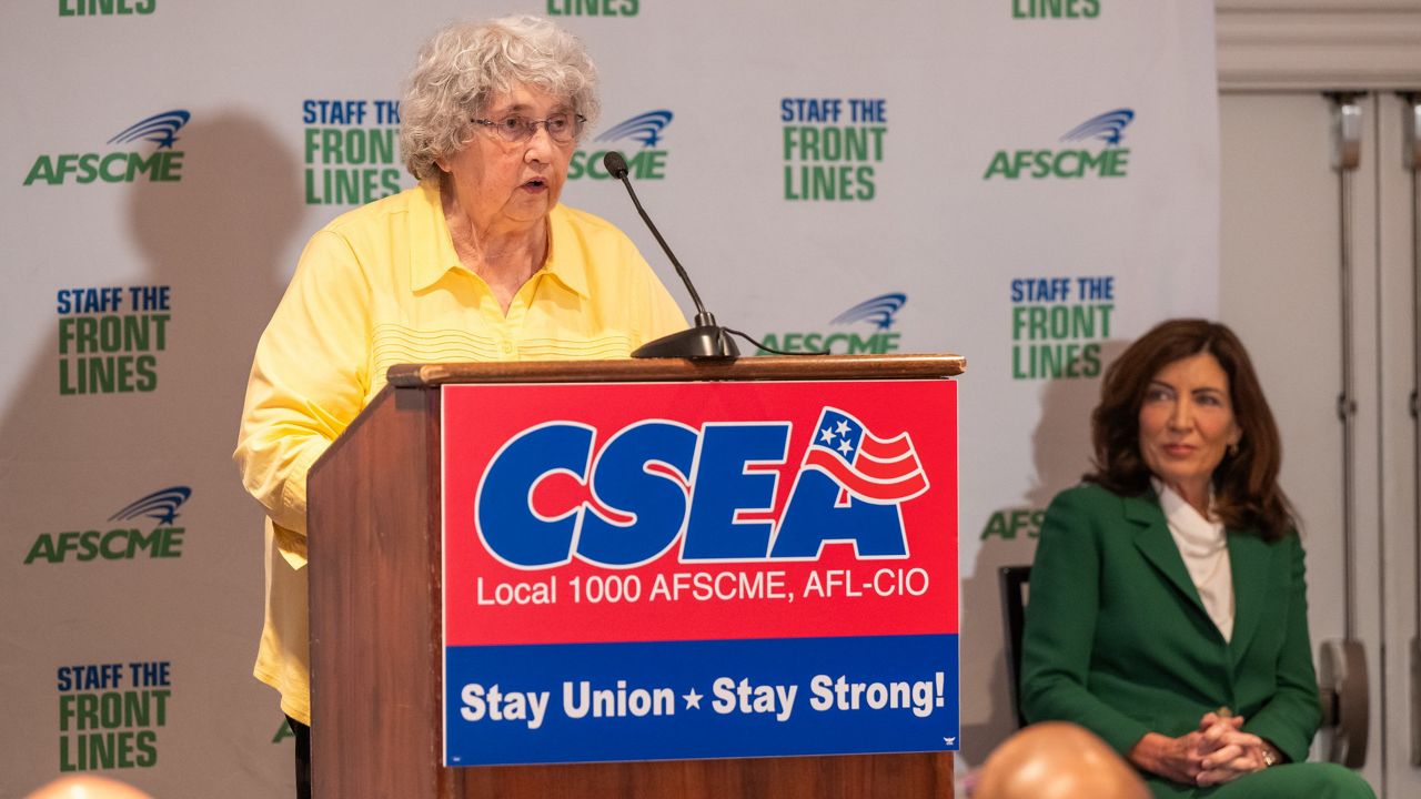 woman speaks at podium alongside governor