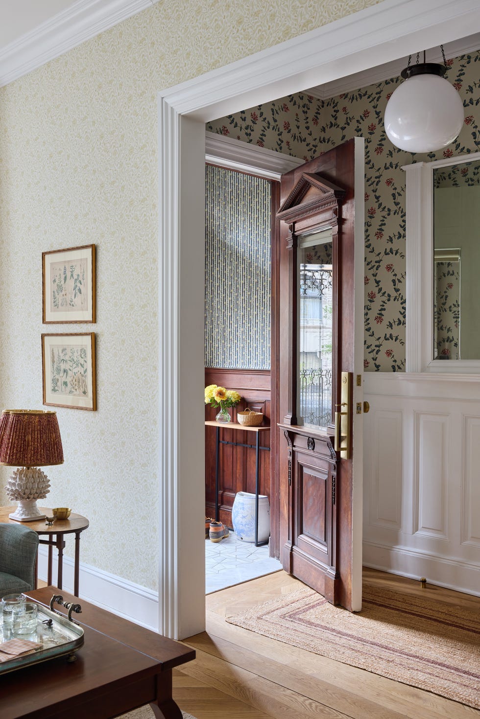 Cozy interior featuring an open door, patterned wallpaper, wooden accents, and a glimpse of a well-decorated space beyond.