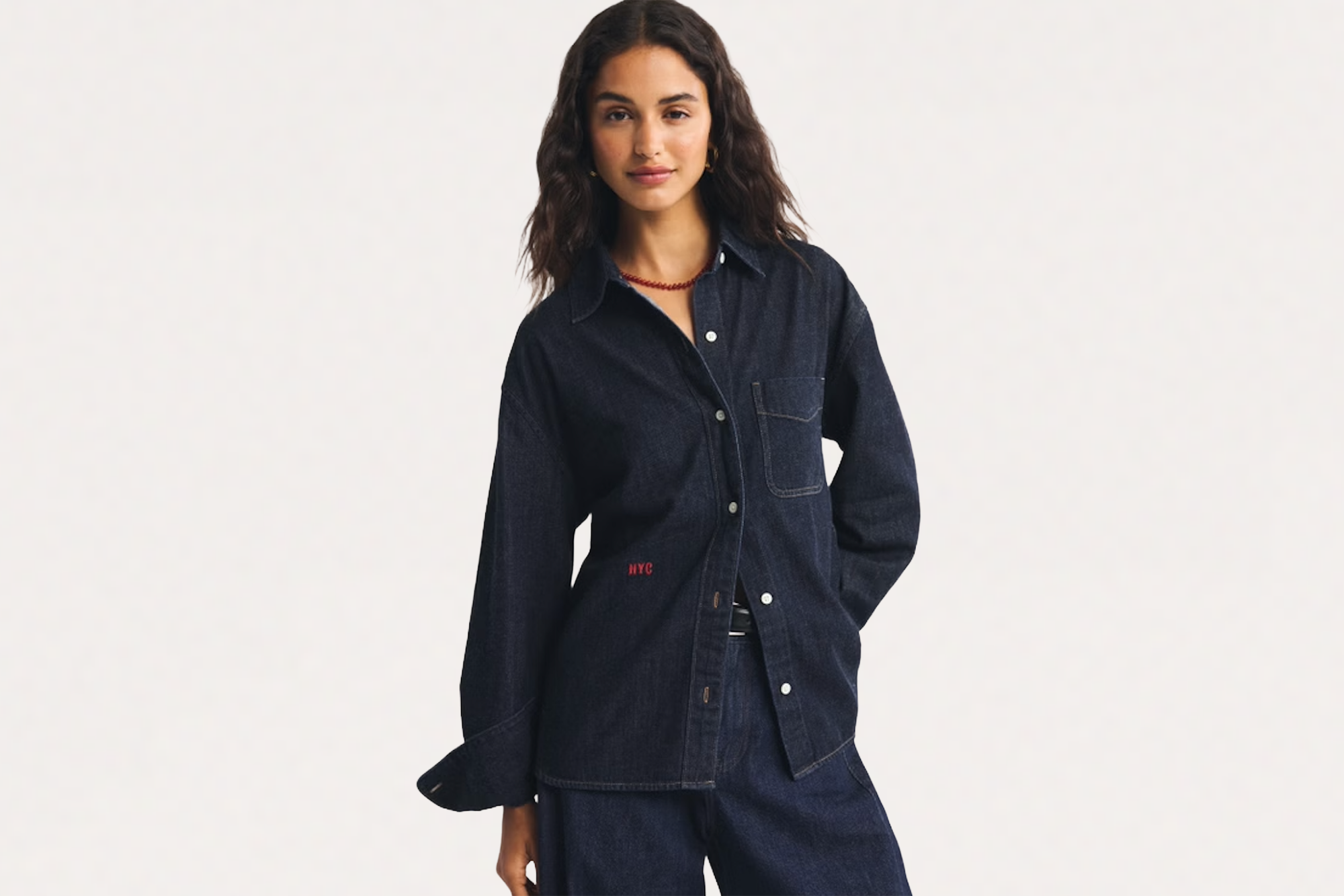 A woman wearing an oversized dark denim shirt with red "NYC" embroidery and dark denim pants.
