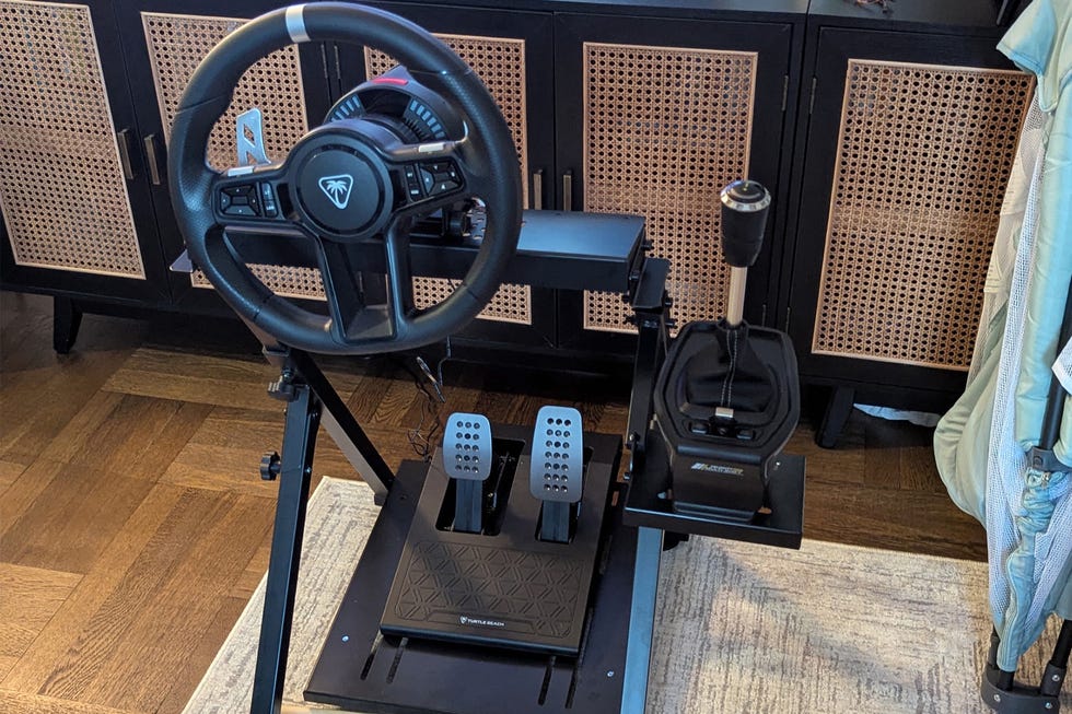 Racing simulation setup featuring a steering wheel, pedals, and gear shifter on a stand.