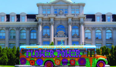 Colorful psychedelic bus with flower patterns in front of a grand stone building.
