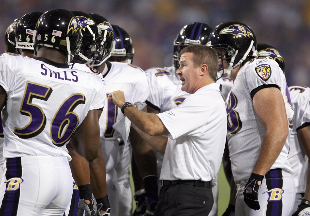 Baltimore Ravens coach speaking to players in a huddle.