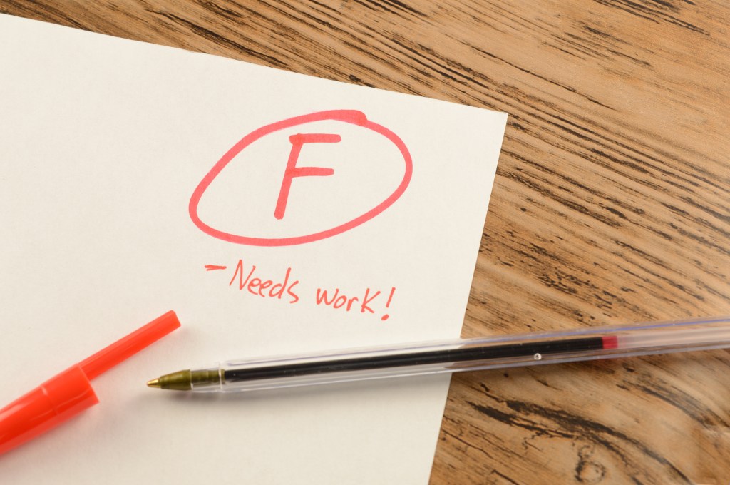 A graded school paper with an "F" and "Needs work!" written in red ink on a wooden desk.
