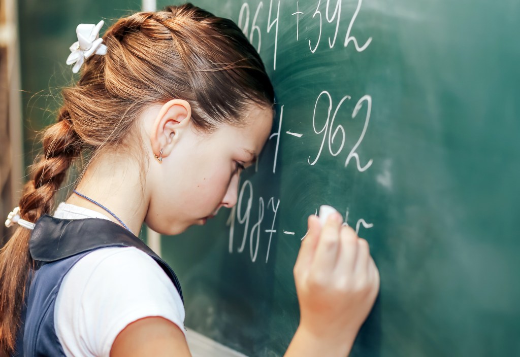 A girl with her head against a chalkboard, doing math.