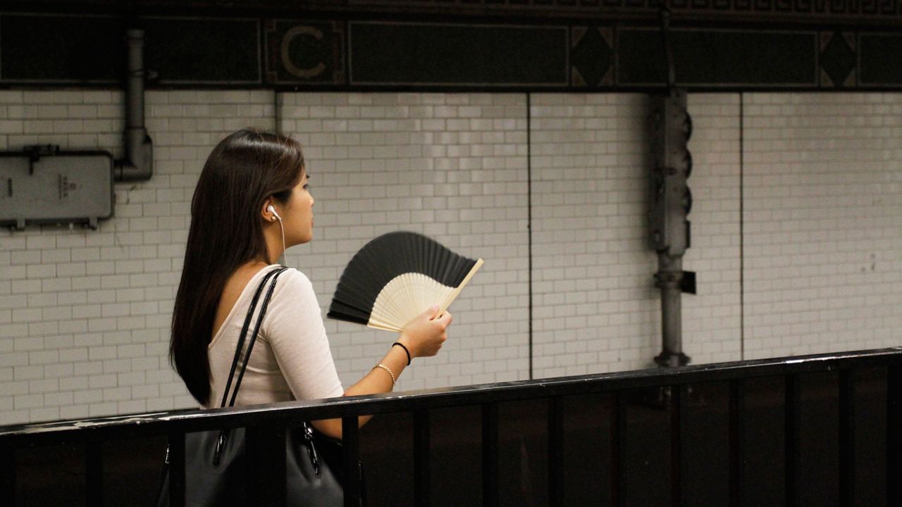 A passenger fans herself as she waits for a train on a sweltering subway platform at Canal Street in New York's Chinatown, Friday, July 19, 2013. A punishing heat wave continues to scorch New York, threatening to break heat records and putting a huge strain on the state s overworked power grid.