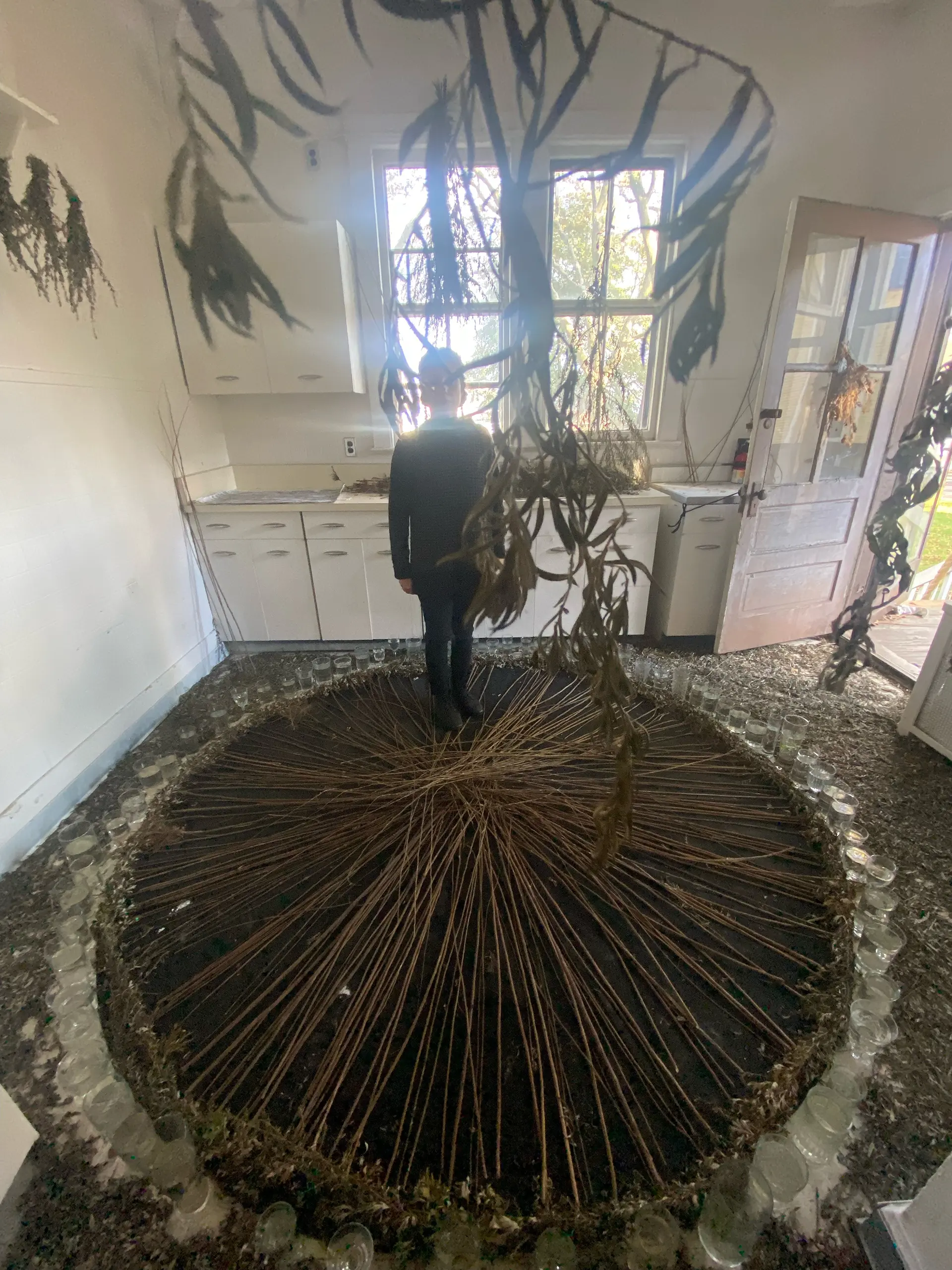 A large, intricate sculpture made of many thin sticks stands in a circular arrangement inside a brightly lit room.