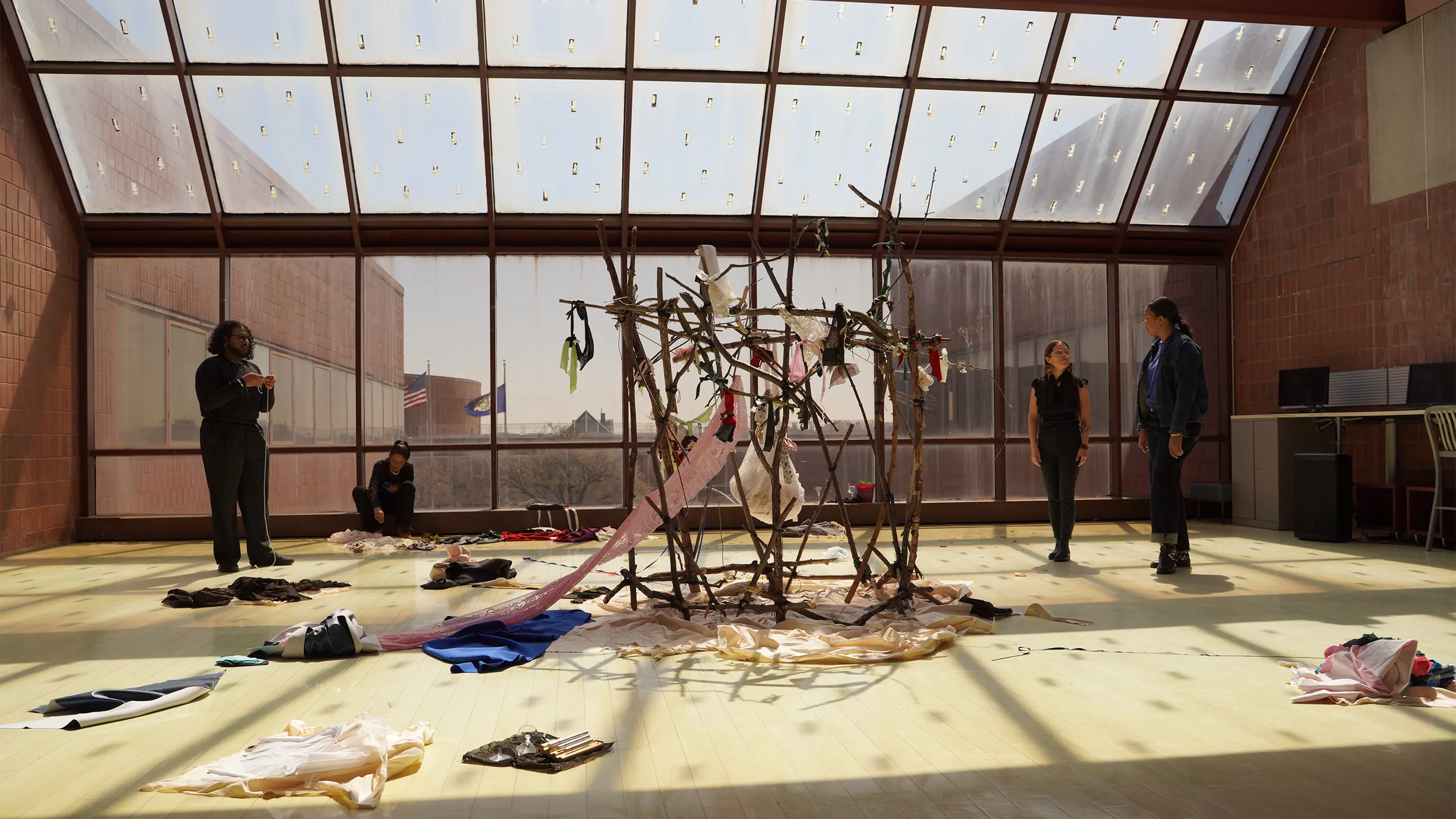 A large, intricate sculpture made of branches and materials sits in a bright, expansive atrium with large windows overlooking a city view.