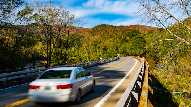 A white car drives down the Catskill Mountain Scenic Byway through fall foliage