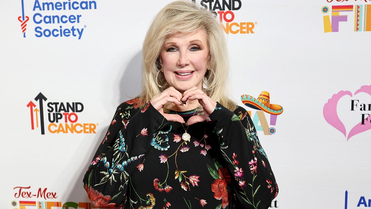 Morgan Fairchild creating a heart symbol with her hands at the red carpet.